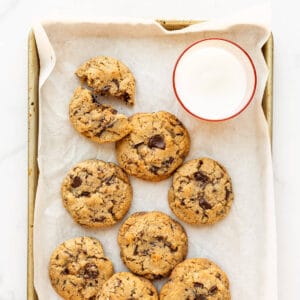 Freshly baked spelt chocolate chip cookies on a sheet pan with a glass of milk.
