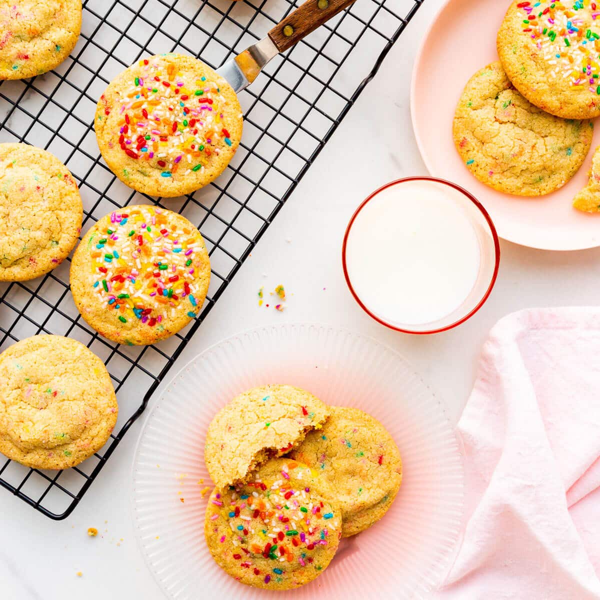 Sprinkle sugar cookies on a cooling rack and on pink plates, served with glasses of milk.