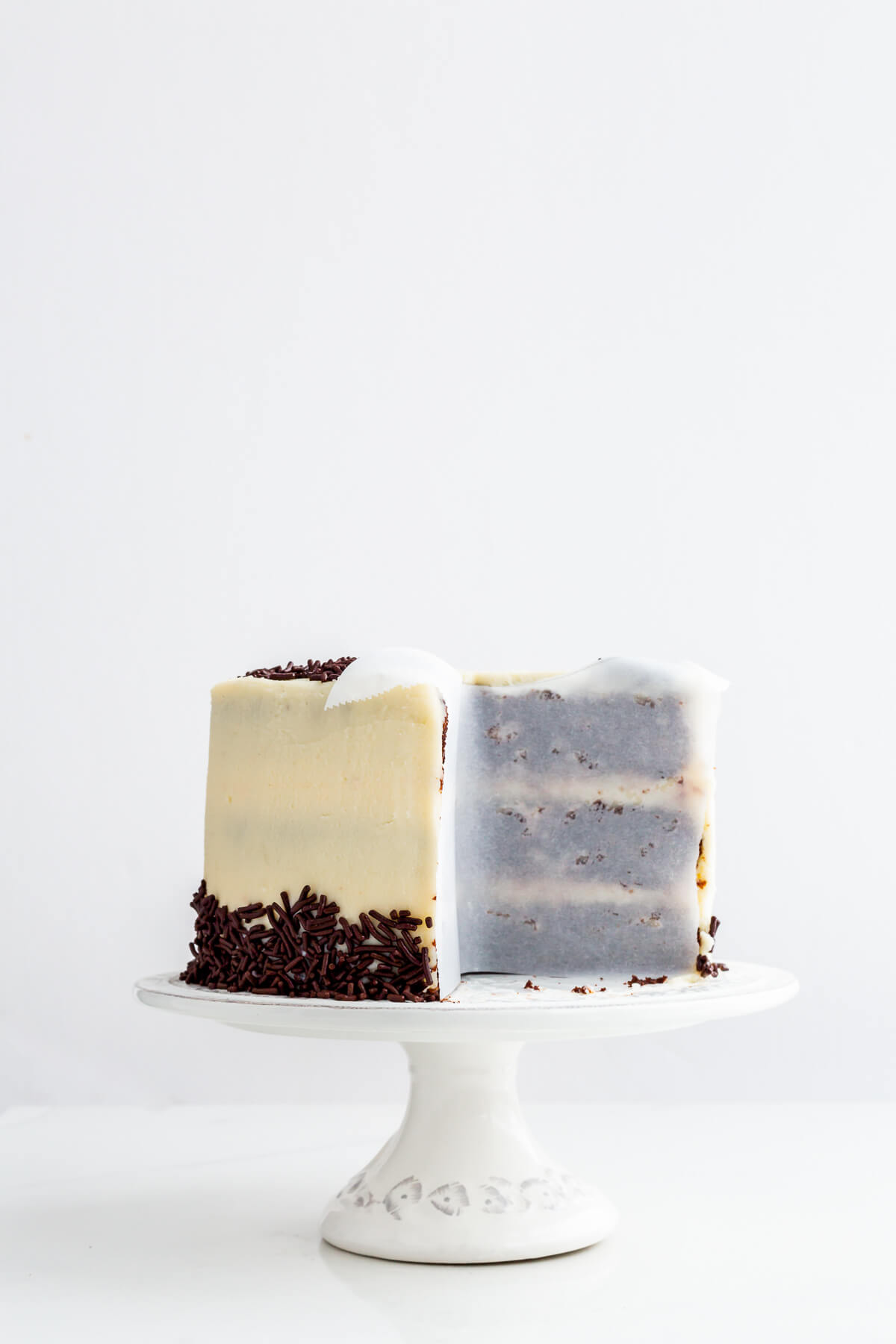 Layer cake on a cake stand with parchment paper to protect the cut edges to prevent drying.