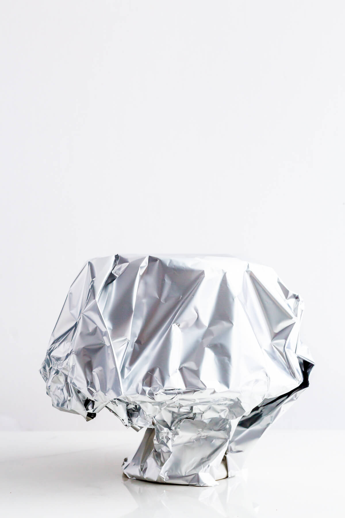 A layer cake on a cake stand, wrapped in aluminum foil to store it in the fridge.