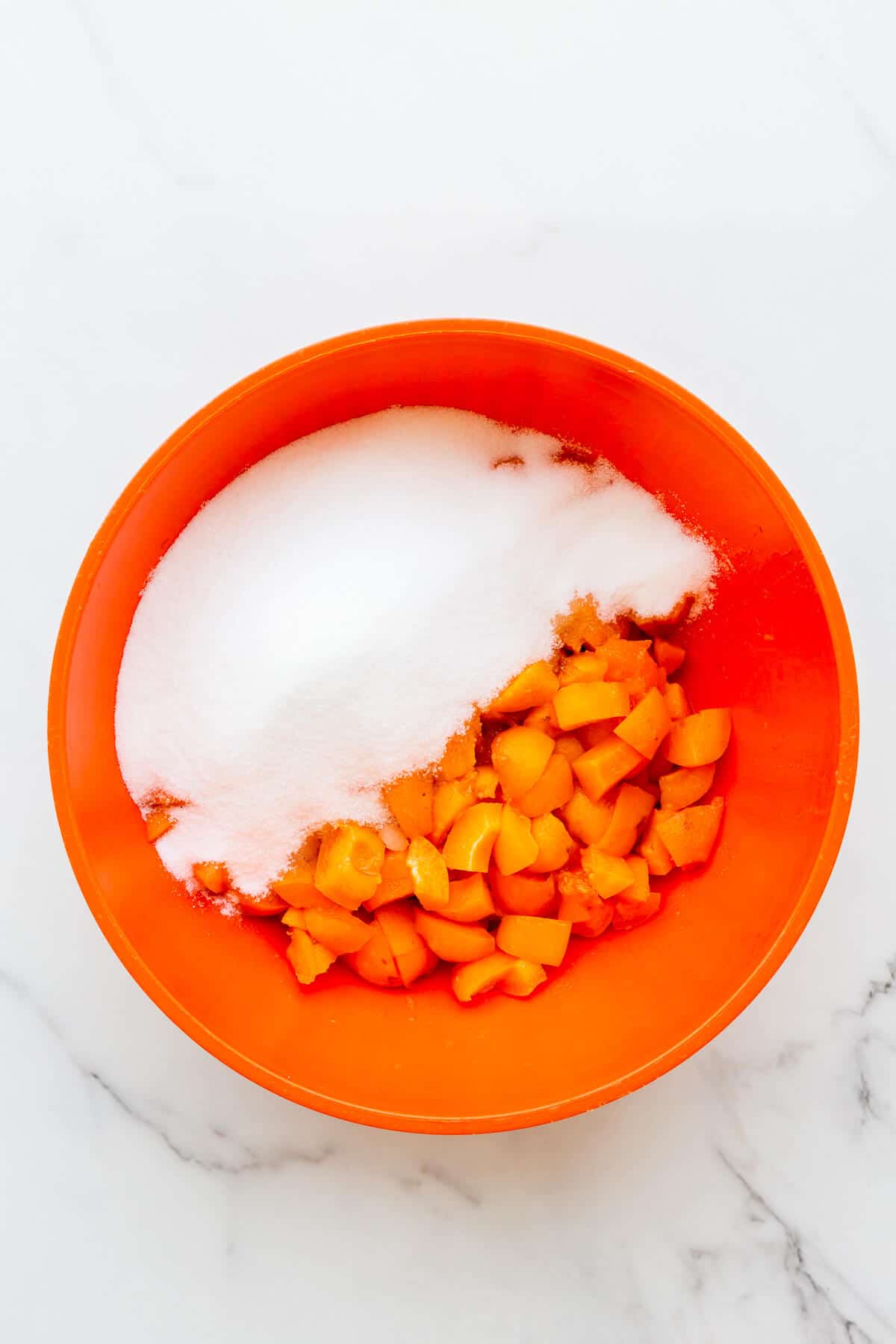 Apricots and sugar ready to be mixed in a bowl to macerate the fruit and extract some of the juices and pectin and to dissolve the sugar before boiling it on the stove to make jam.