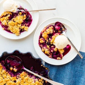 Serving apple and blueberry crumble with scoops of vanilla ice cream on plates.