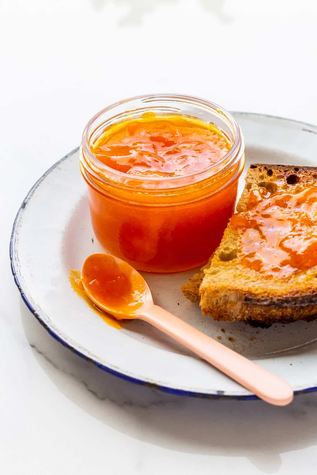 Toast with a jar of apricot jam on a plate.