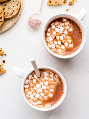 Cups of hot cocoa with cookies and mini marshmallows.