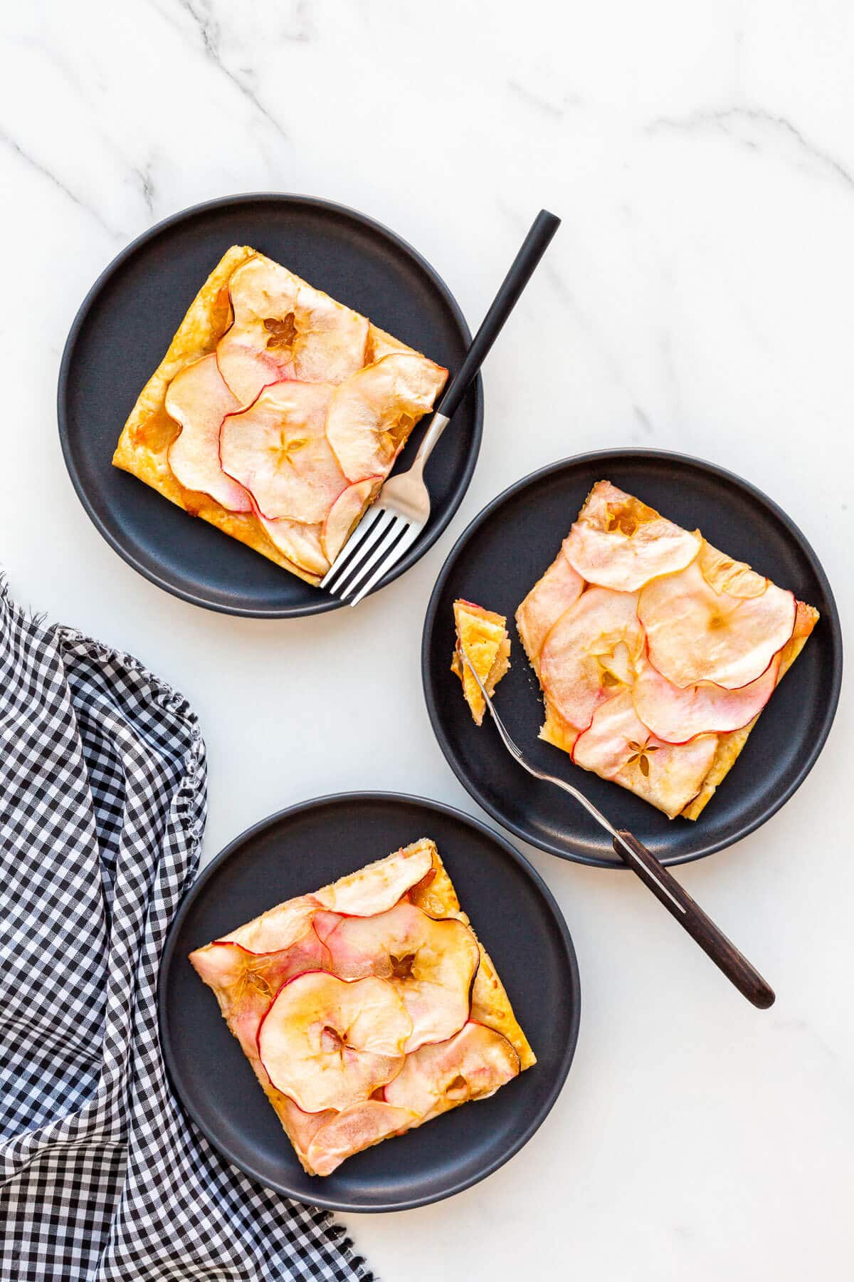 Squares of apple tart on black plates ready to be eaten.