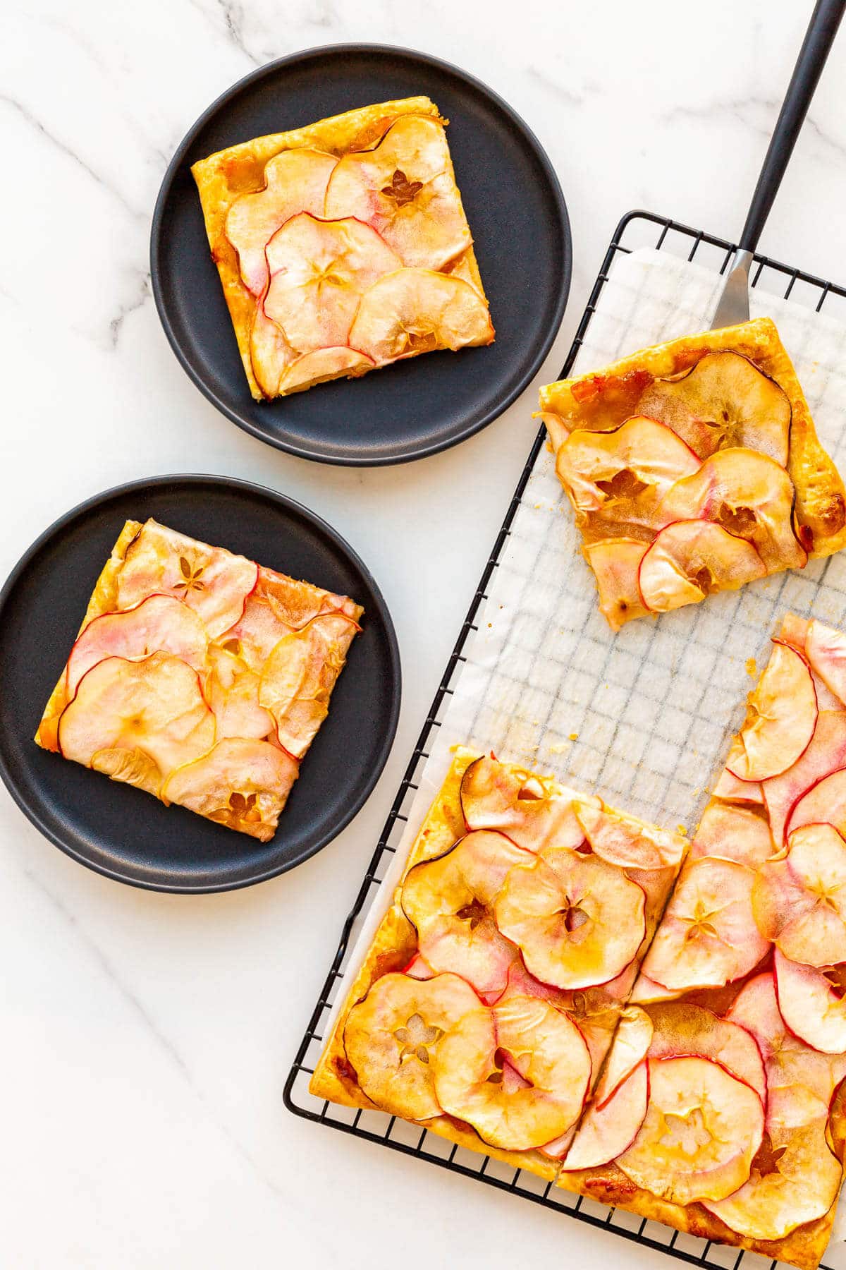 Puff pastry apple tart cut into squares to serve on plates.