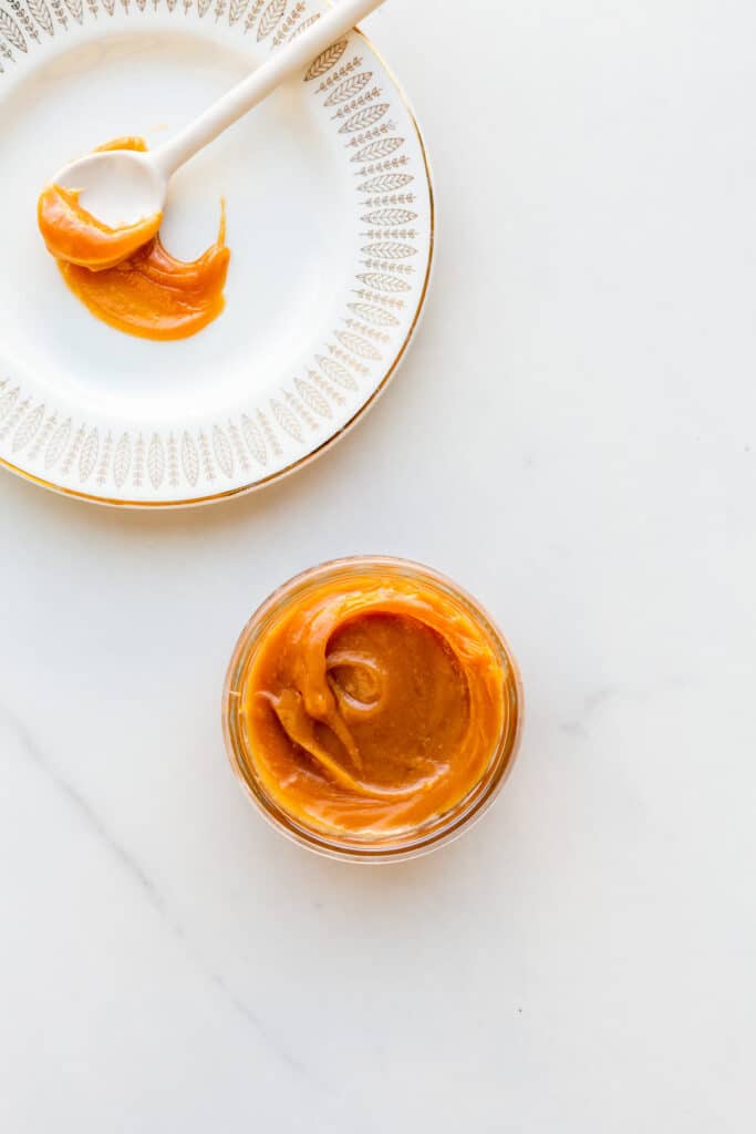 A jar of thick dulce de leche with a plate and a spoon on the side.