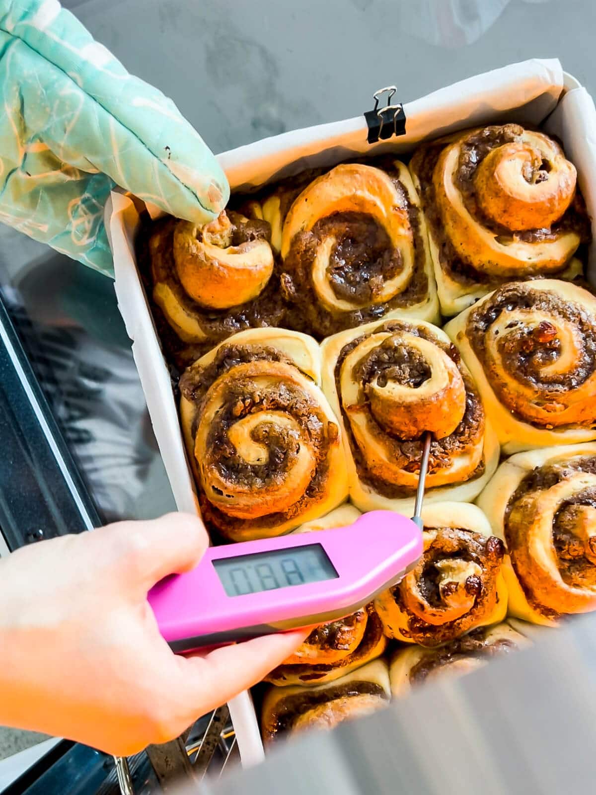 Checking the internal temperature of cinnamon rolls with an instant-read digital thermometer to make sure they are baked in the middle.