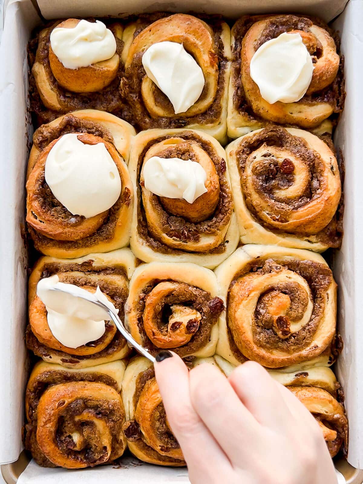 Dolloping cream cheese icing on warm cinnamon rolls to frost them before enjoying.