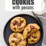 A plate of chocolate chip cookies with pecans and chunks of milk chocolate served with a glass of milk.