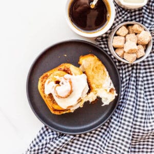 A cinnamon raisin bun on a black plate being eaten, with a cup of coffee on the side.