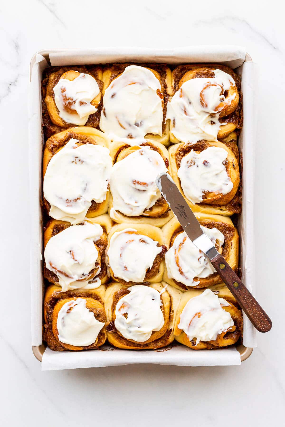 Frosting freshly baked cinnamon rolls with cream cheese icing and a mini offset spatula.