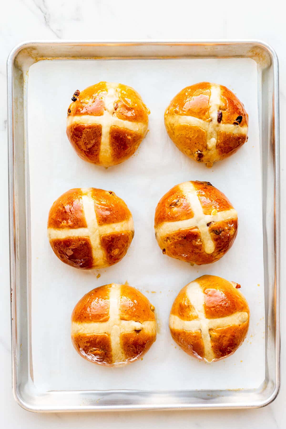 Hot cross buns on a sheet pan after baking in the oven.