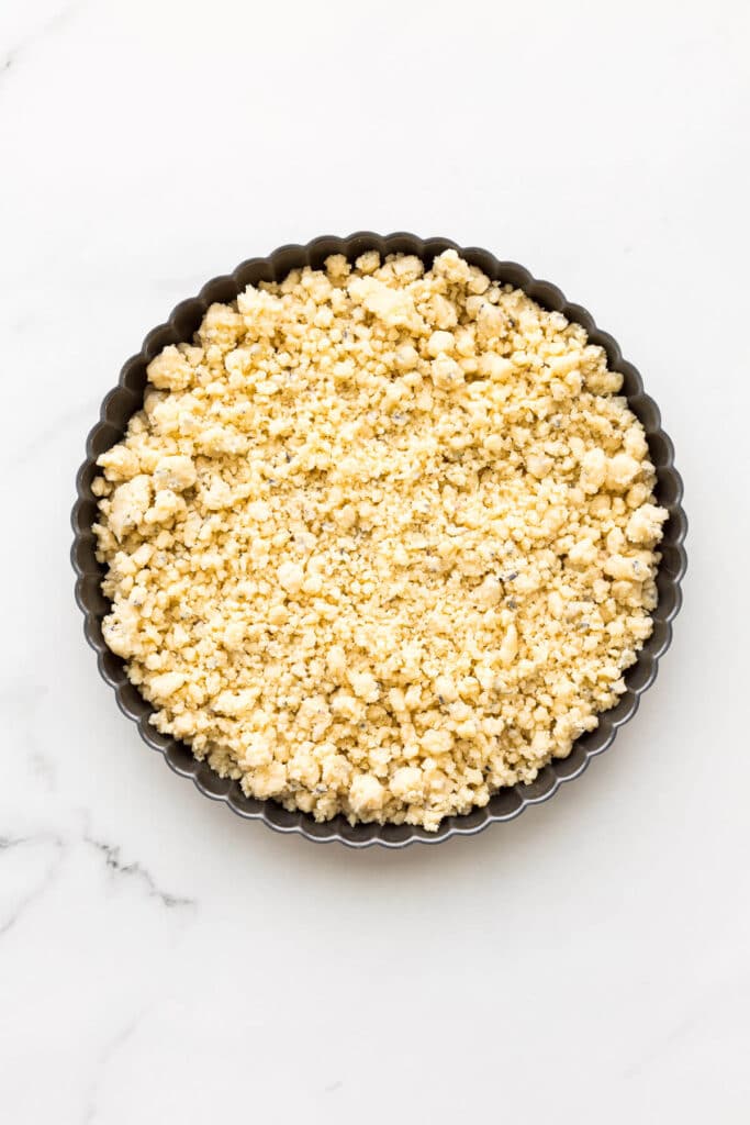 Crumbly shortbread cookie dough in a pan, ready to be pressed into place to smooth it out before baking.