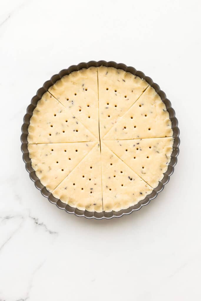 Lavender shortbread cookies in a tart pan cut into wedges before baking.