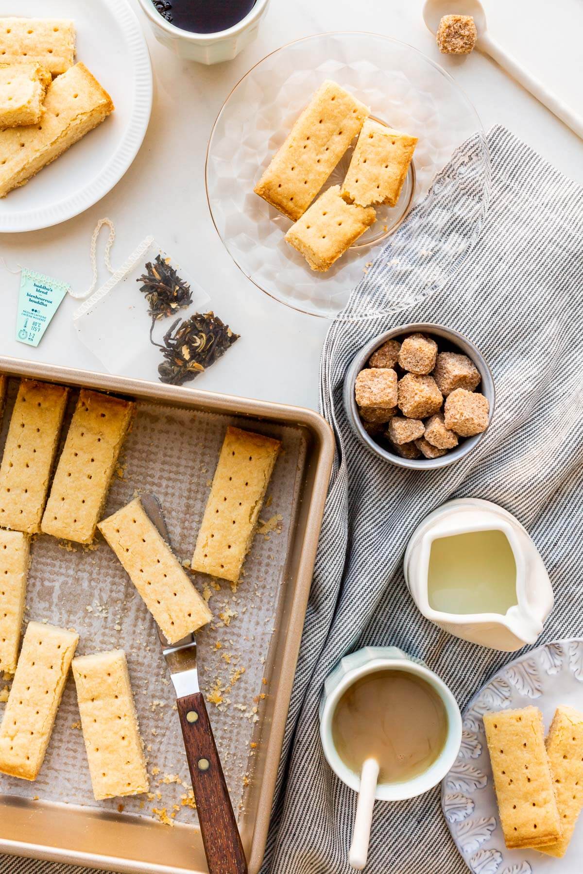 Shortbread cookies being served on small plates with cups of tea, milk, and sugar cubes.