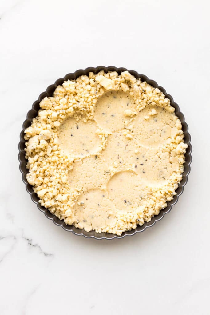 Shortbread cookie dough pressed into a tart pan before baking, using a flat-bottomed glass to create a smooth surface.