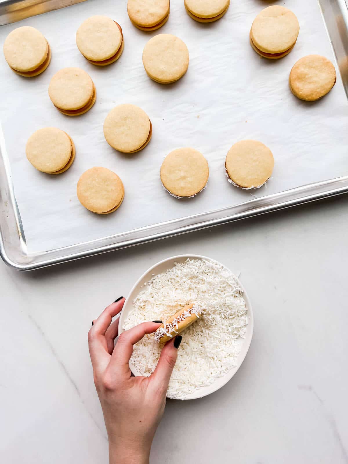 Rolling alfajores cookies in a bowl of coconut to coat the edges.