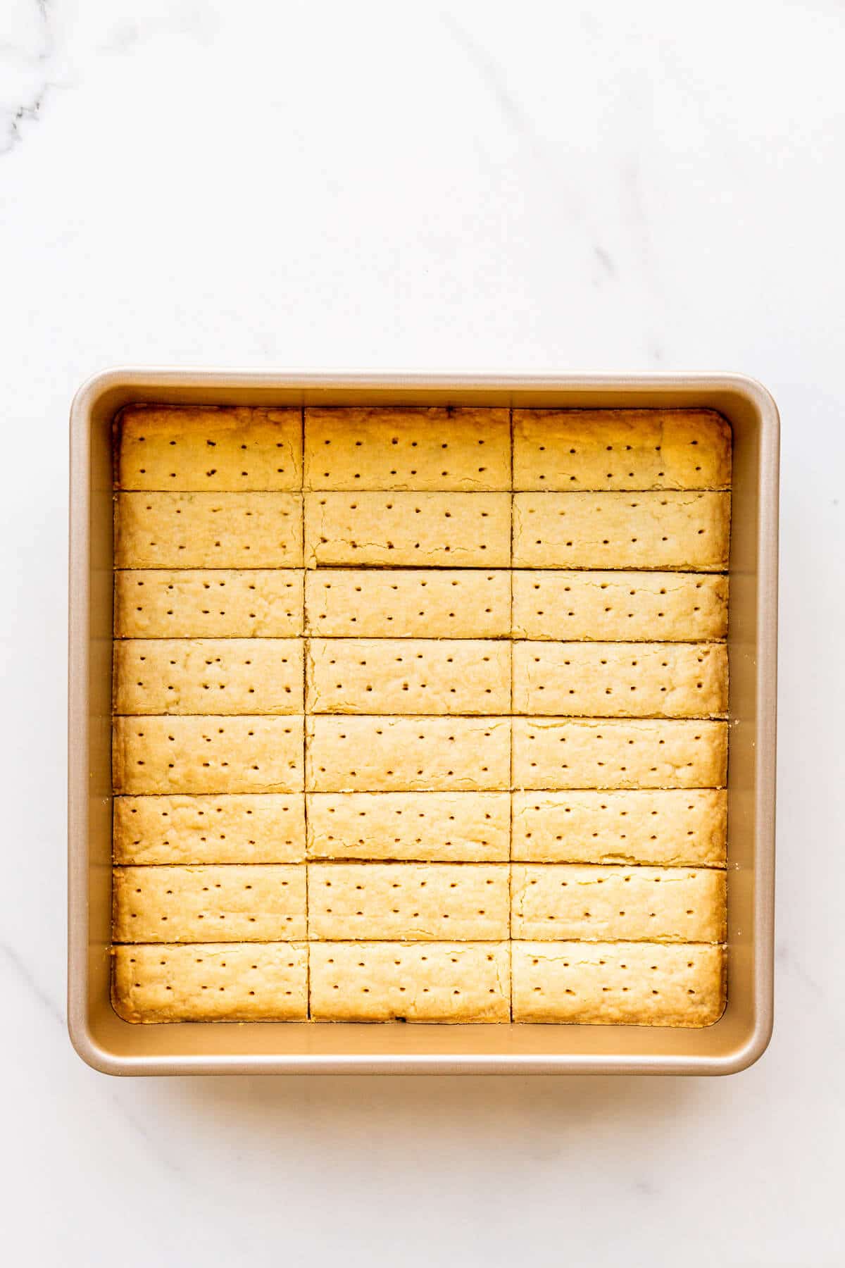 Freshly baked shortbread cookies in a square baking pan, cut into sticks and ready to unmould.