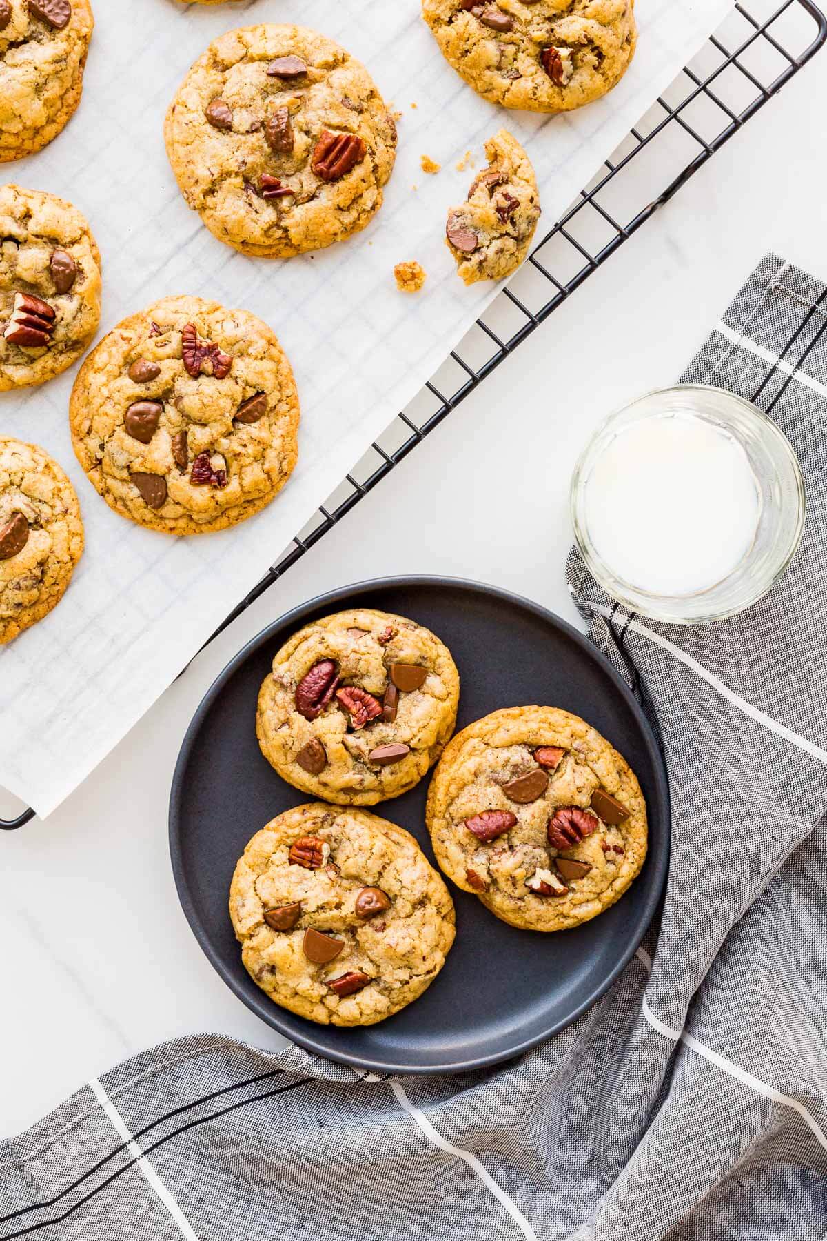 Milk chocolate chip cookies with pecans being served on a black plate from a cooling rack.