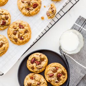 Chocolate chip cookies with pecans cooled on a rack being served on black plates with glasses of milk.