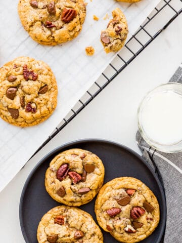 Chocolate chip cookies with pecans cooled on a rack being served on black plates with glasses of milk.