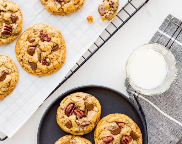 Chocolate chip cookies with pecans cooled on a rack being served on black plates with glasses of milk.