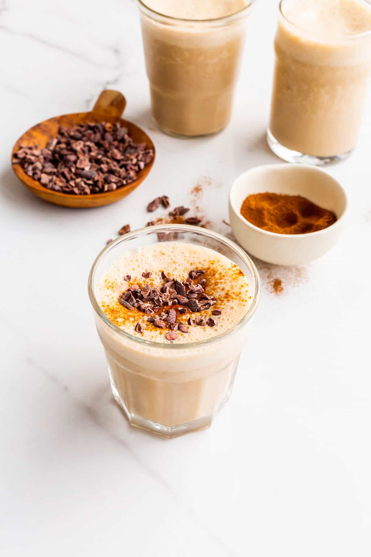 Small glasses of coffee banana smoothie topped with espresso powder and cocoa nibs.
