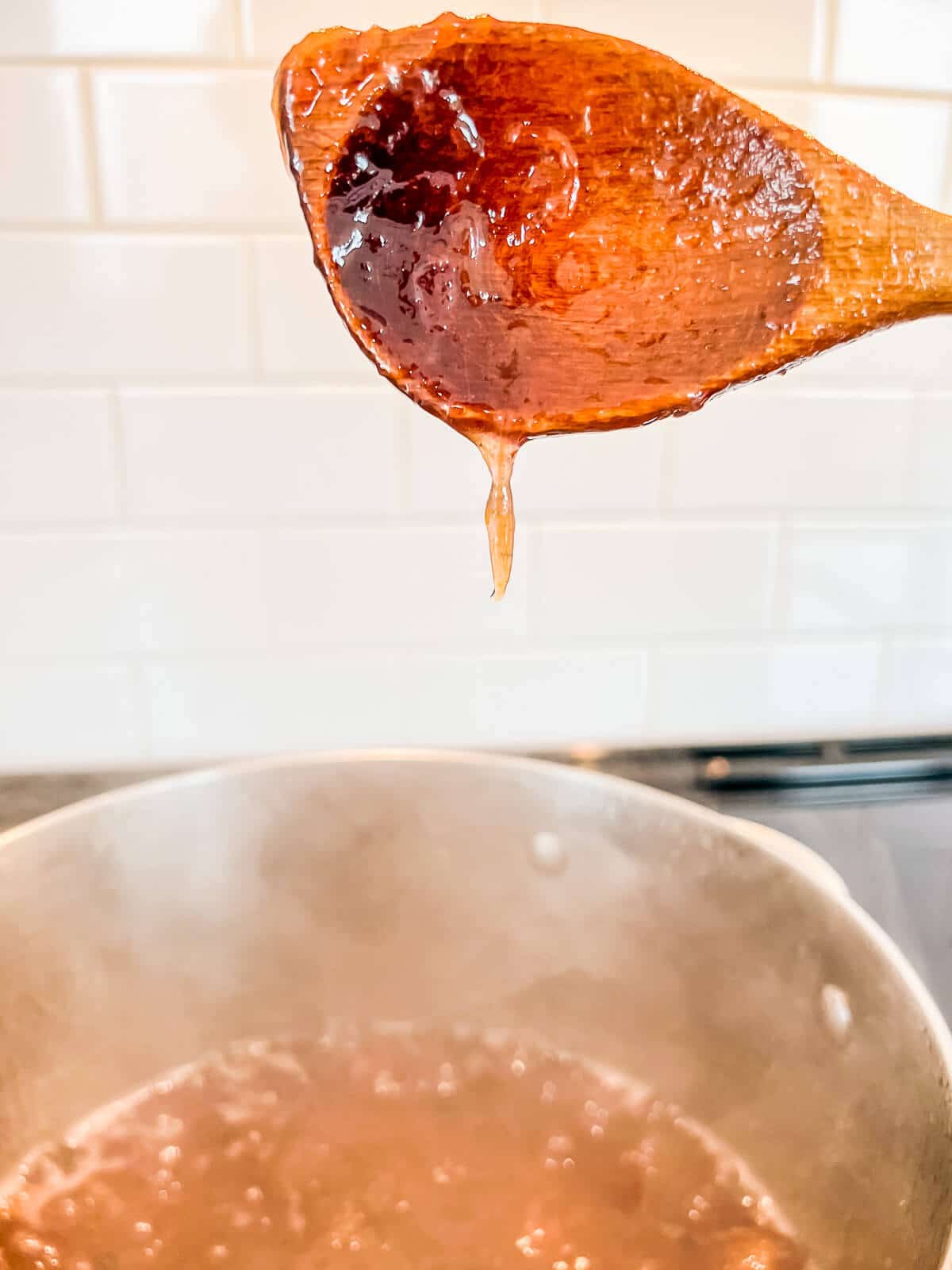 Checking the set of a pot of boiling jam by lifting the wooden spoon to see how it drips.