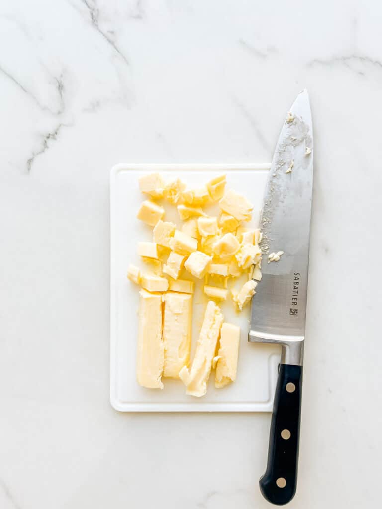 Chopping cold butter into pieces to soften it faster for baking.