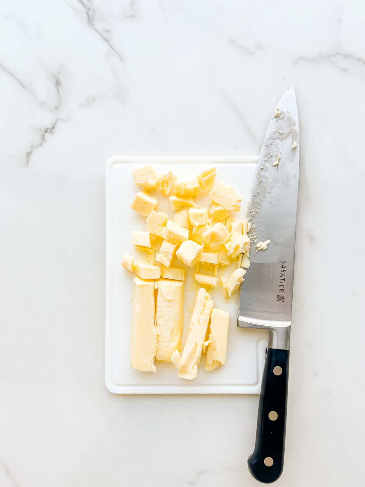 Chopping cold butter into pieces to soften it faster for baking.