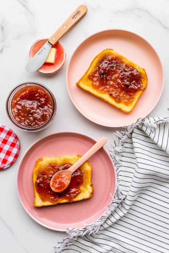 Two pink plates with toast, served with butter and jam.