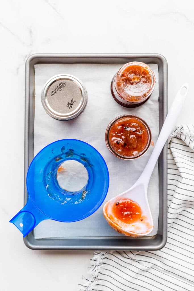 Filling sterilized jars with homemade jam using a blue non-reactive plastic funnel and a white ladle.