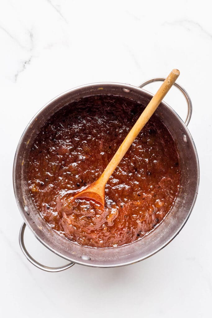 A pot of homemade rhubarb jam boiled to the jam setting point, stirred with a wooden spoon.