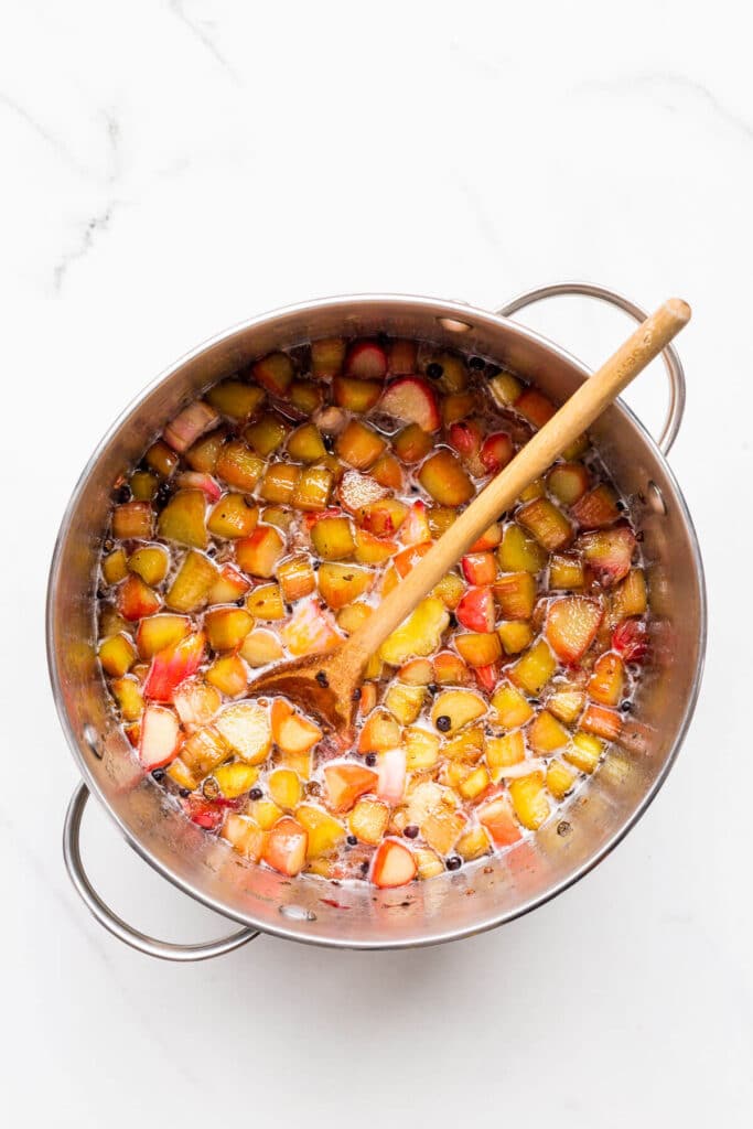 A pot of homemade rhubarb jam before boiling to the jam setting point, stirred with a wooden spoon.