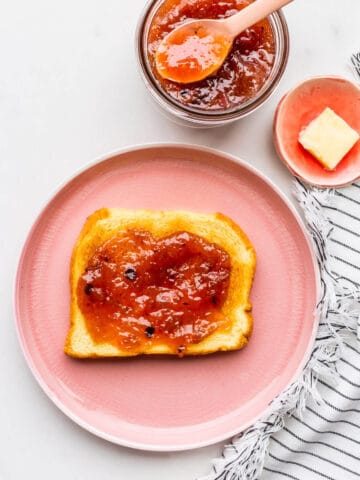 A pink plate with a piece of toast topped with homemade rhubarb jam.