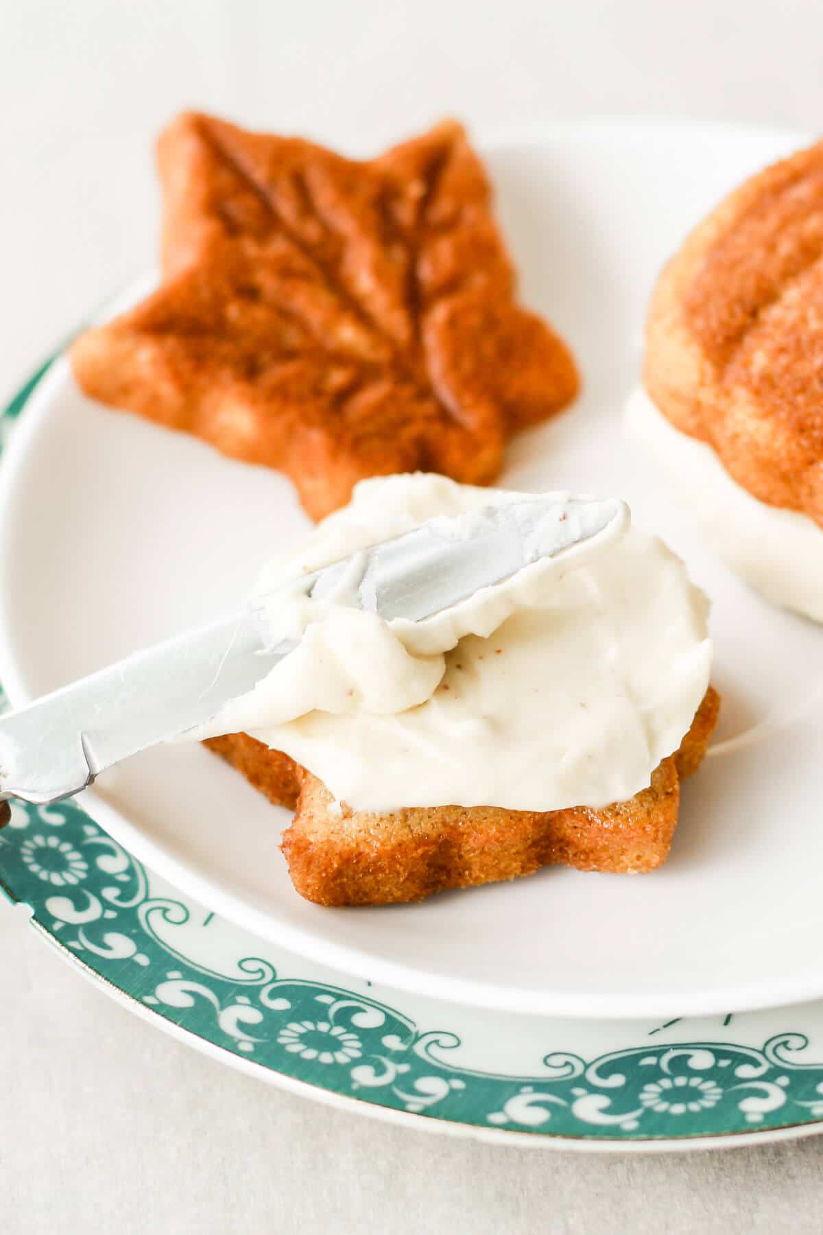 Pumpkin whoopie pies being filled with brown butter cream cheese frosting, spreading it on with a knife.