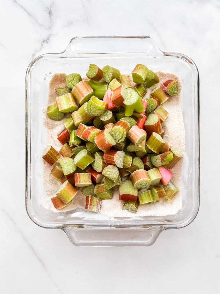 A glass baking dish with chopped rhubarb, sugar, and tapioca starch, ready to be roasted.