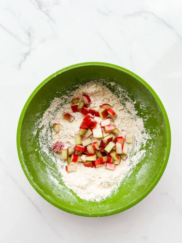 Adding chopped rhubarb to dry ingredients and butter to incorporate it into scones