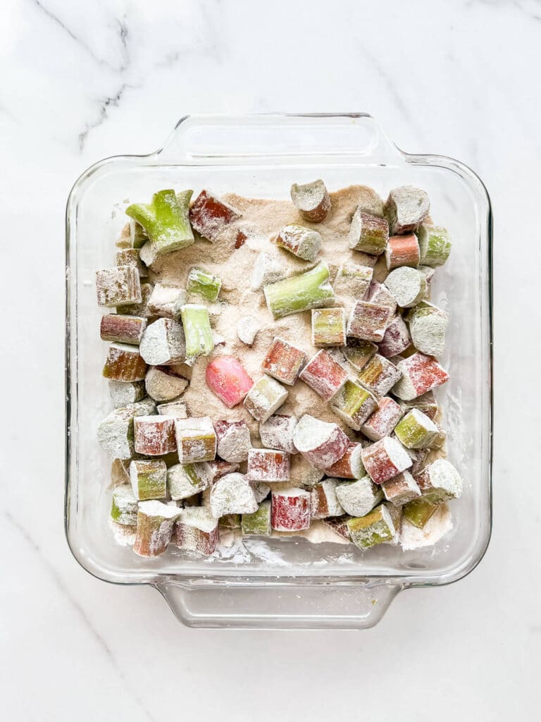 A glass baking dish with chopped rhubarb stirred with sugar and tapioca starch, ready to be baked.