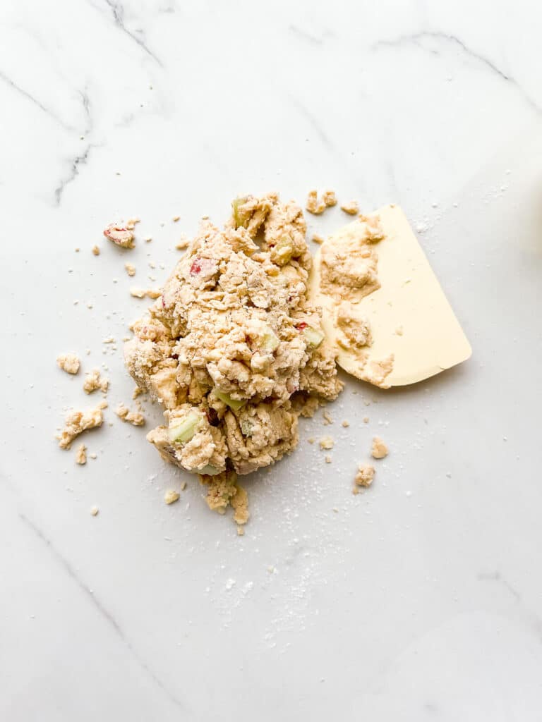 Using a bench scraper to pull together scone dough into a cohesive dough mass.