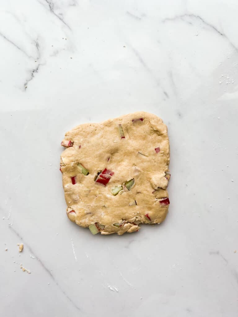 Scone dough with rhubarb patted out into a square to cut out scones.