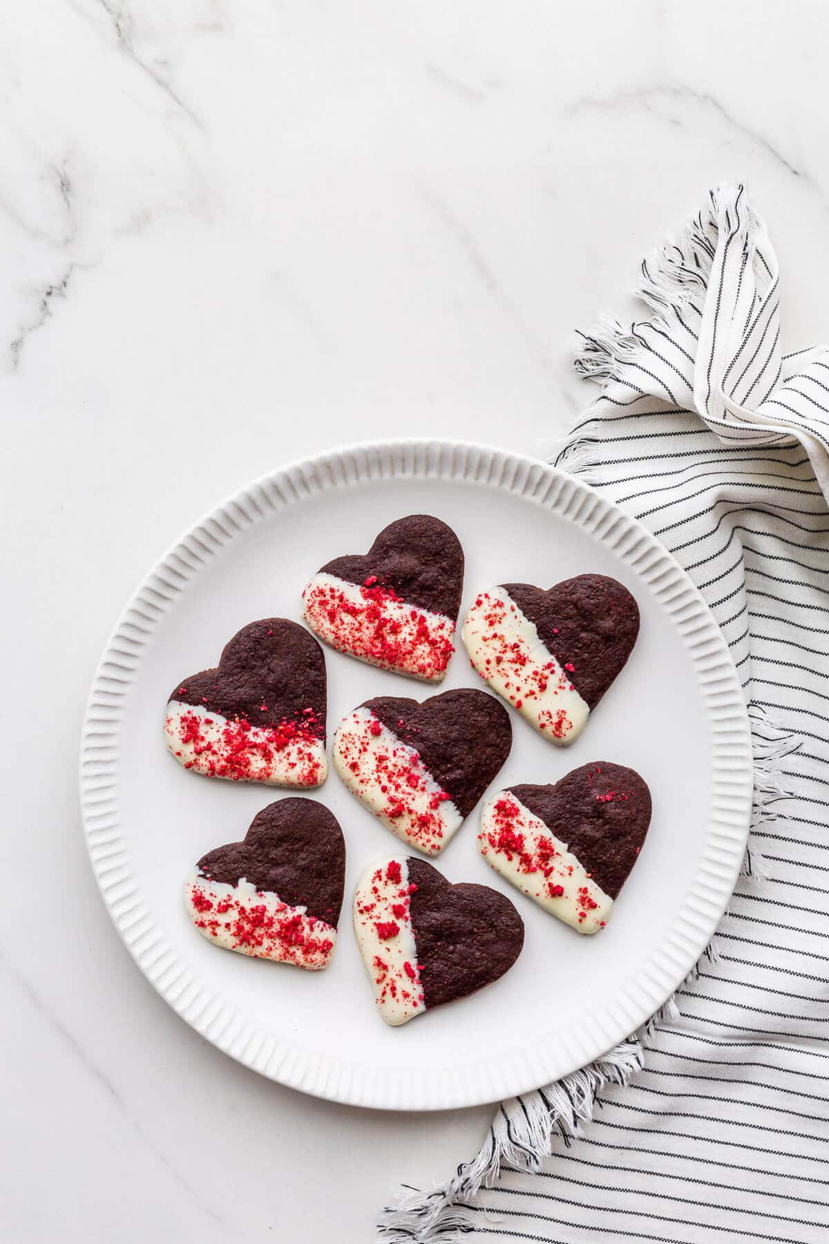 A plate of cutout chocolate shortbread cookies dipped in white chocolate and sprinkled with freeze-dried raspberries.