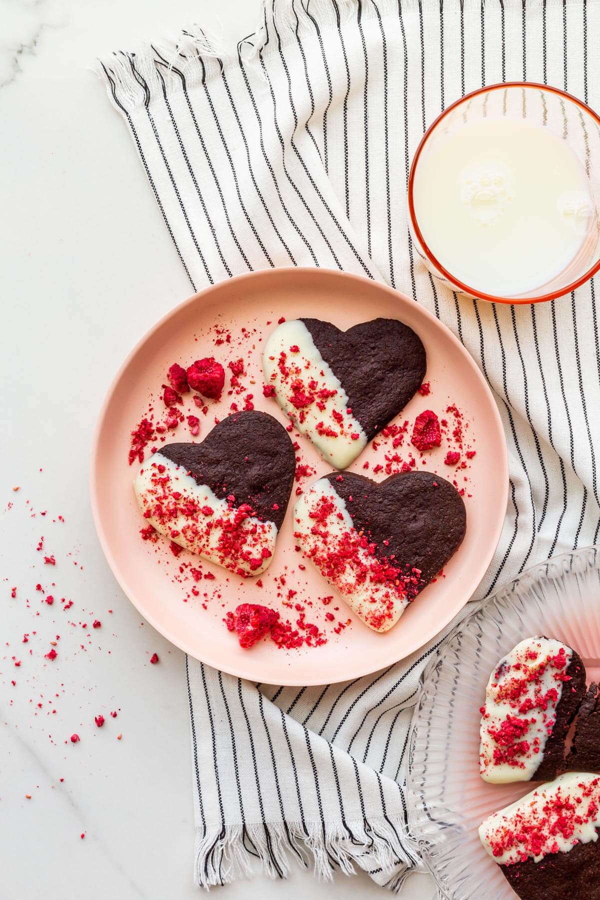 A plate of chocolate shortbread cookies that are dipped in white chocolate and sprinkled with crushed freeze-dried raspberries.