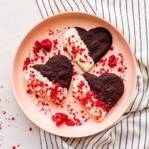 A plate of chocolate shortbread cookies that are dipped in white chocolate and sprinkled with crushed freeze-dried raspberries.