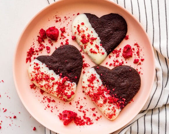 A plate of chocolate shortbread cookies that are dipped in white chocolate and sprinkled with crushed freeze-dried raspberries.