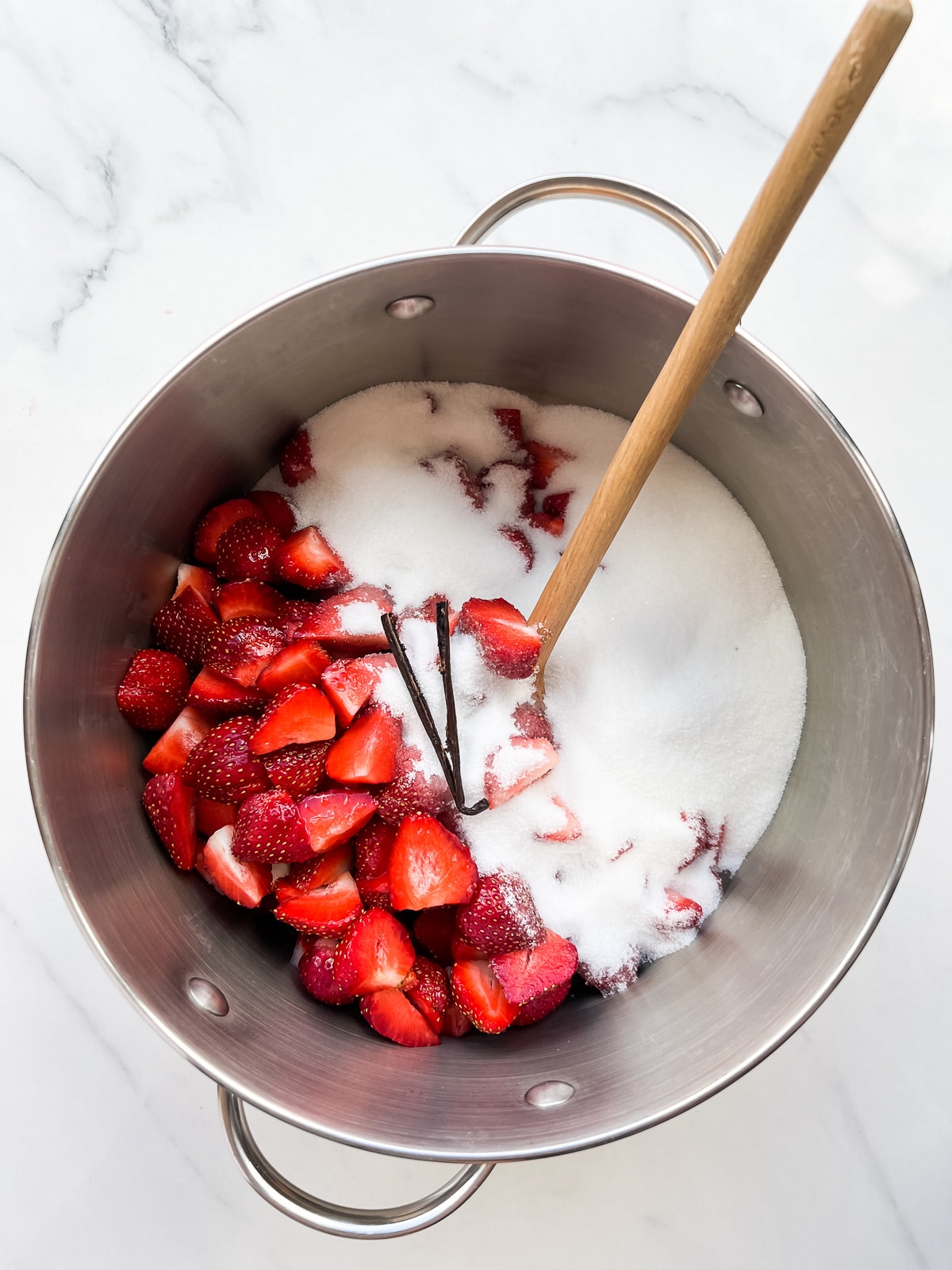 Combining sliced strawberries with sugar and a vanilla bean to macerate before making homemade jam.