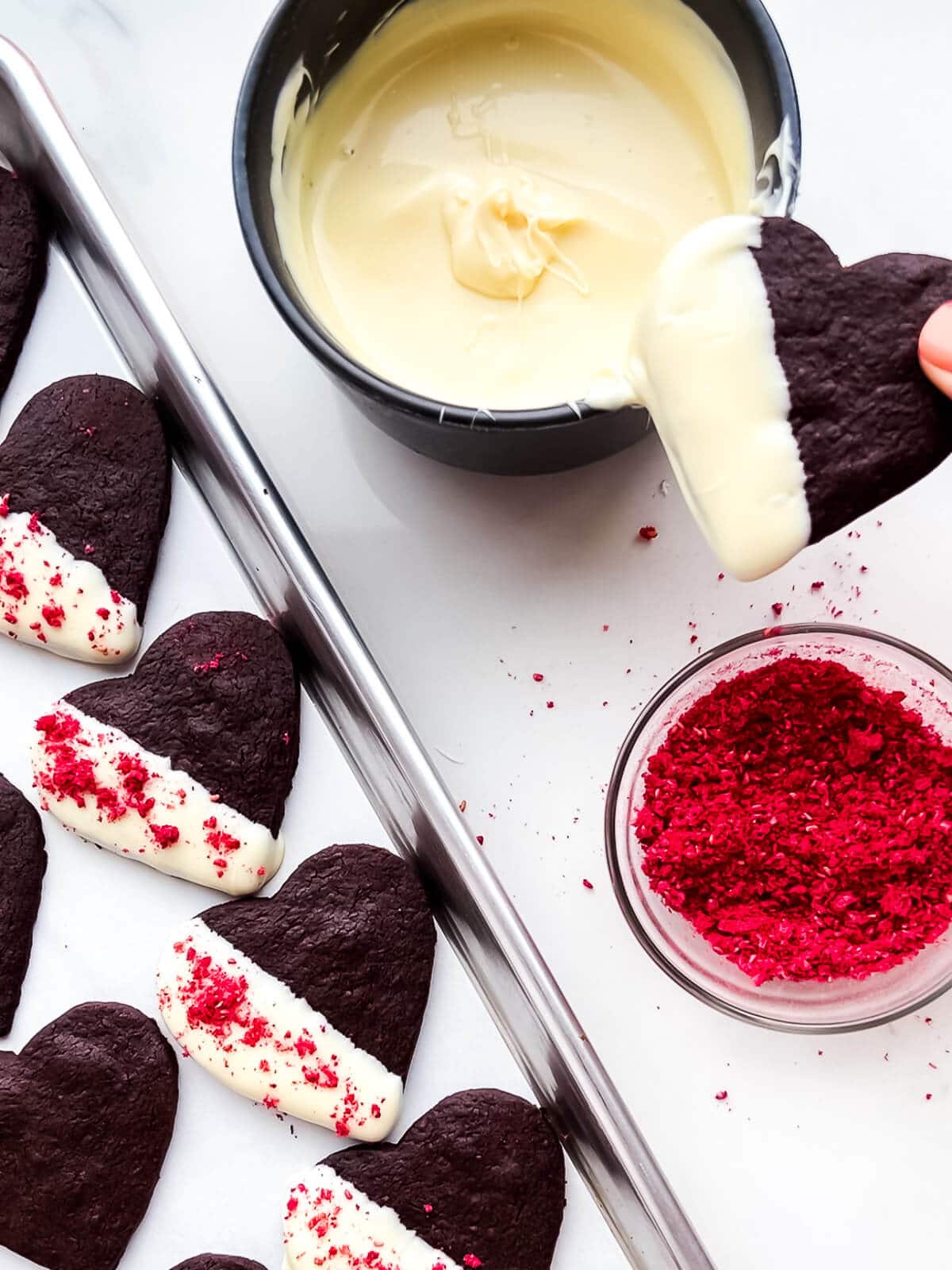 Dipping chocolate shortbread cookies in white chocolate and sprinkling with crushed freeze-dried raspberries.