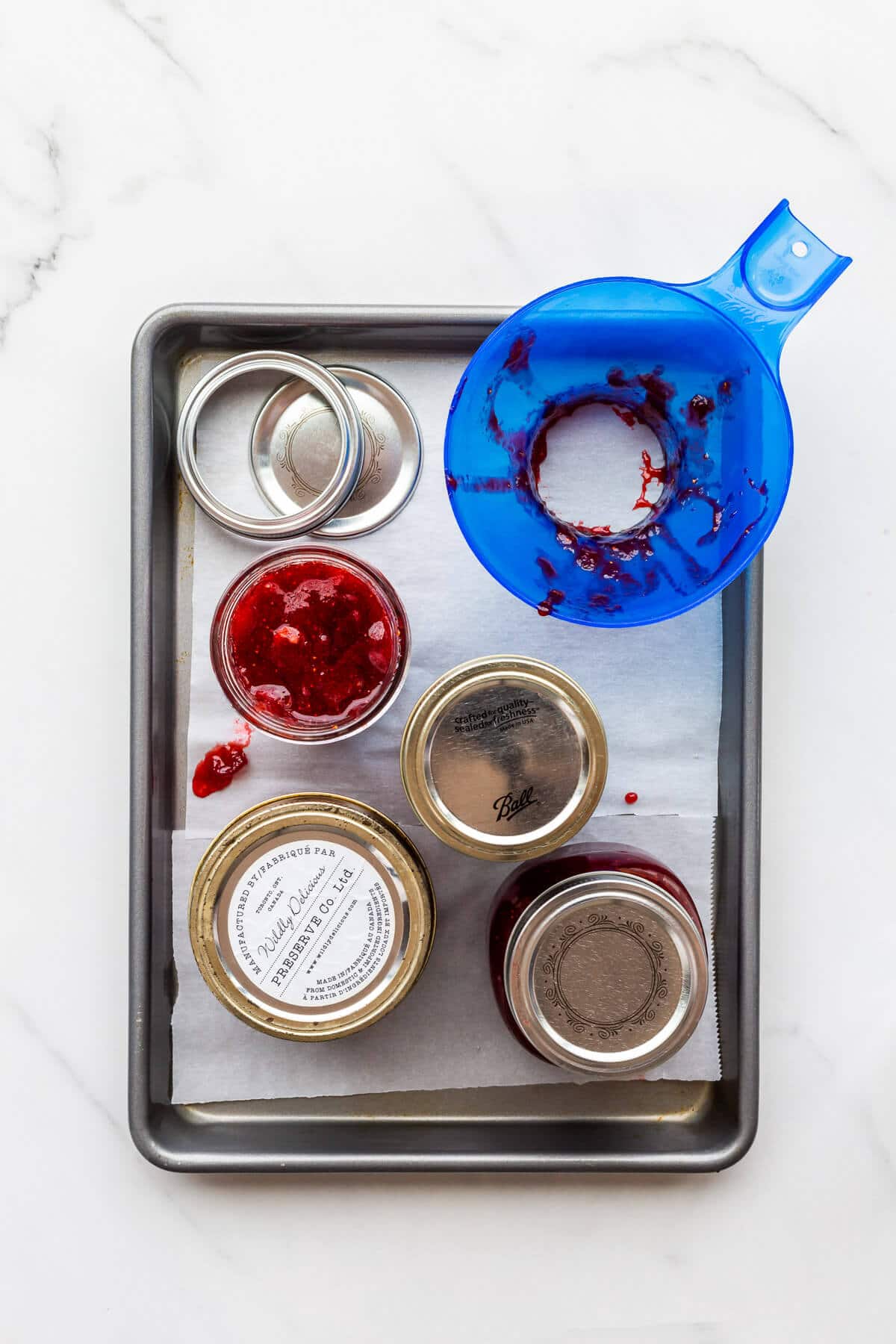 Filling jars with homemade strawberry rhubarb jam to seal them and store for later.