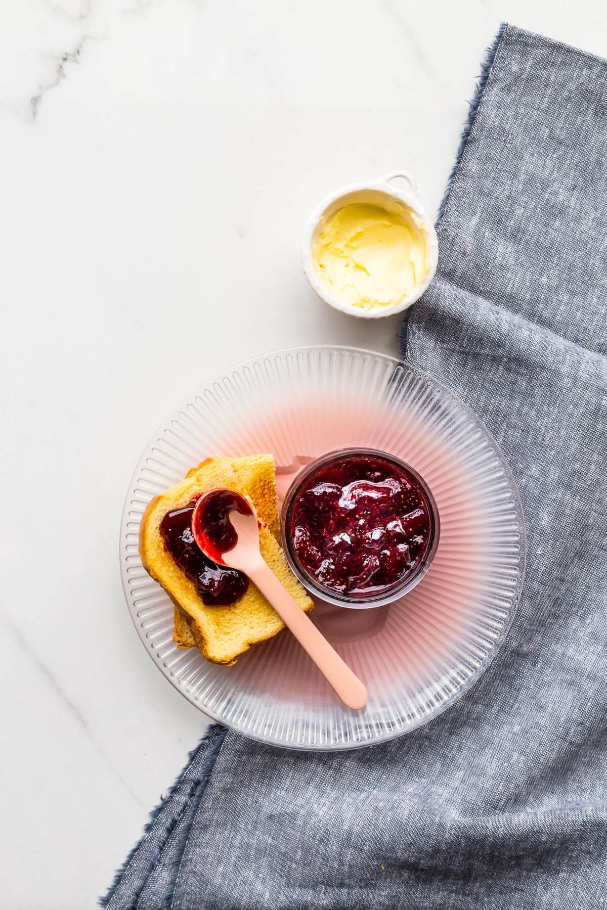 A jar of strawberry jam served with toast on a plate.